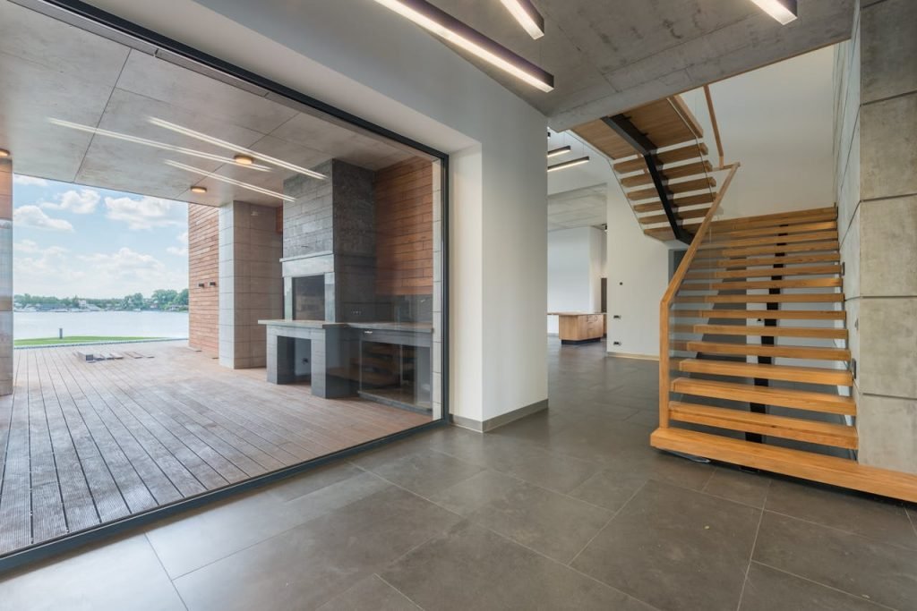 Spacious interior with wooden staircase and exit to terrace in loft apartment on daytime