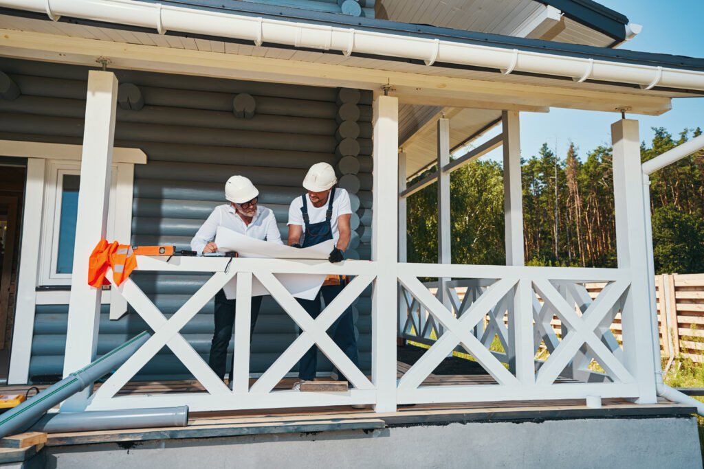 Structural engineer and construction person in safety caps leaning over paper layout and discussing building process
